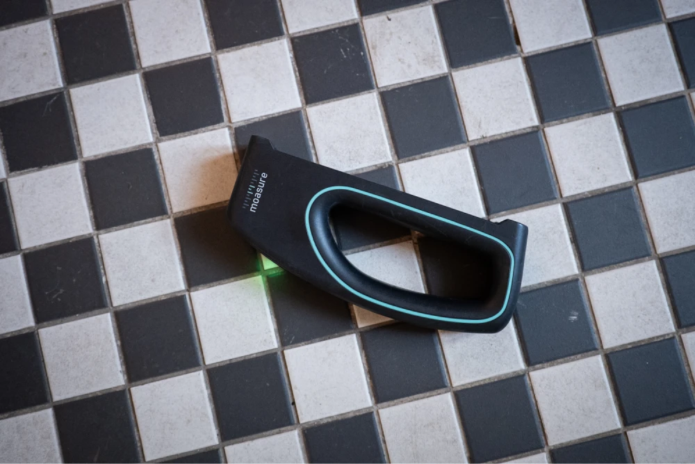 Moasure LX1 lying on a black and white tiled floor, its laser lit